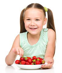 Image showing Cheerful little girl is eating strawberries