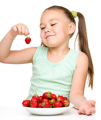 Image showing Cheerful little girl is eating strawberries