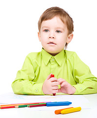 Image showing Little boy is drawing on white paper using crayon