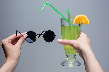 Image showing The female hands with cocktail and sunglasses on gray background