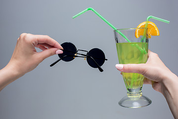 Image showing The female hands with cocktail and sunglasses on gray background