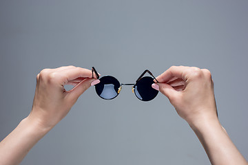 Image showing The female hands holding sunglasses on gray background.