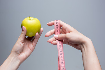 Image showing Green apple in female hands on gray background. Weight loss, diet