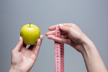Image showing Green apple in female hands on gray background. Weight loss, diet
