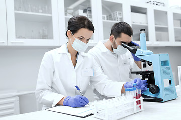 Image showing scientists with clipboard and microscope in lab