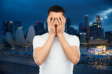 Image showing man in white t-shirt covering his face with hands