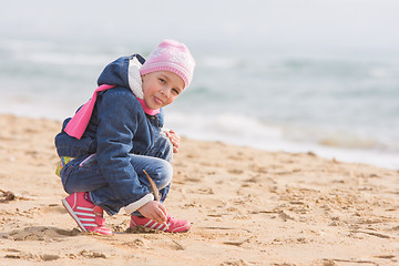 Image showing Five-year girl in the spring of the pen draws on the sand by the sea, and has shown language in the frame