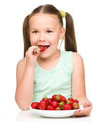 Image showing Happy little girl is eating strawberries