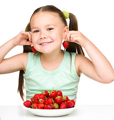 Image showing Cheerful little girl is eating strawberries