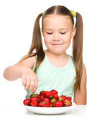 Image showing Happy little girl is eating strawberries