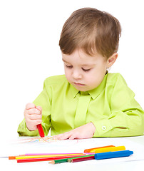 Image showing Little boy is drawing on white paper using crayon