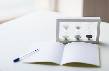 Image showing close up of notebook, pen and hourglass on table