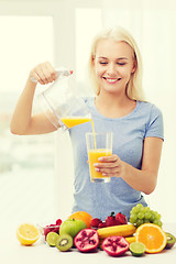 Image showing smiling woman pouring fruit juice to glass at home