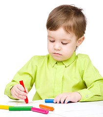 Image showing Little boy is drawing on white paper using crayon