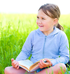 Image showing Little girl is reading a book outdoors