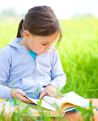 Image showing Little girl is reading a book outdoors