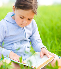 Image showing Little girl is reading a book outdoors