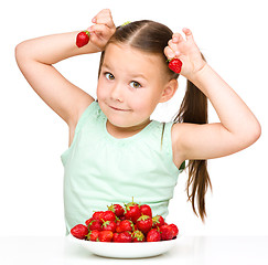 Image showing Happy little girl is eating strawberries