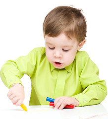 Image showing Little boy is drawing on white paper using crayon