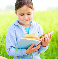 Image showing Little girl is reading a book outdoors