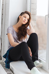 Image showing sad pretty teenage girl sitting on windowsill