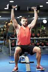 Image showing young man with dumbbells flexing muscles in gym