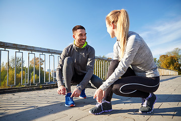Image showing smiling couple tying shoelaces outdoors