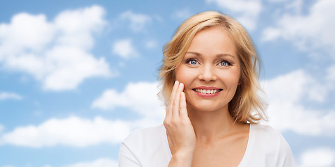 Image showing smiling woman in white t-shirt touching her face