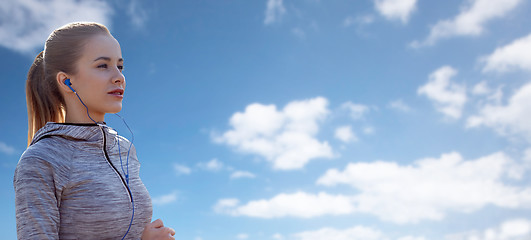 Image showing happy woman with earphones running over blue sky