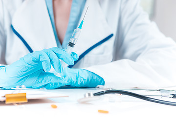 Image showing The hand in blue glove holding syringe against white medical gown 