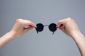 Image showing The female hands holding sunglasses on gray background.