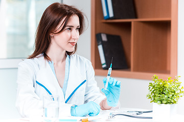 Image showing The hand in blue glove holding syringe against white medical gown 