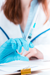 Image showing The hand in blue glove holding syringe against white medical gown 