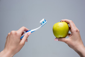 Image showing Toothbrush and apple in woman\'s hands on gray