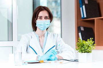 Image showing The hand in blue glove holding syringe against white medical gown 