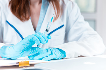 Image showing The hand in blue glove holding syringe against white medical gown 