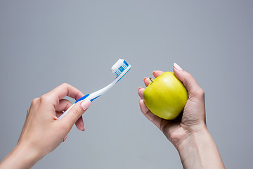 Image showing Toothbrush and apple in woman\'s hands on gray