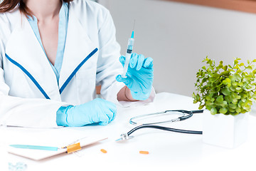 Image showing The hand in blue glove holding syringe against white medical gown 