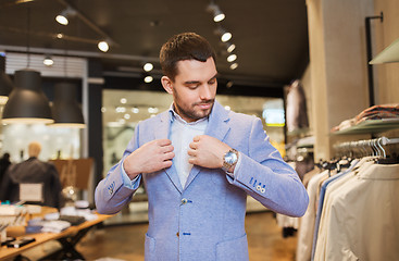 Image showing happy young man trying jacket on in clothing store