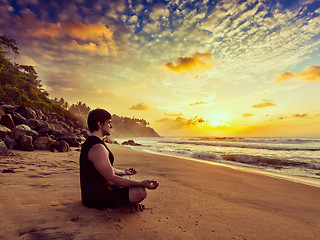 Image showing Young sporty fit man doing yoga meditating on tropical beach