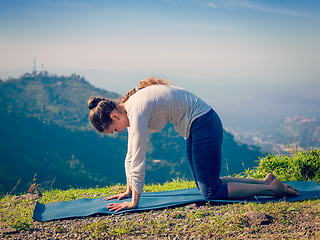 Image showing Sporty fit woman practices yoga asana Marjariasana outdoors