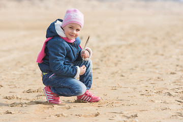 Image showing Five-year girl sat down on the sand by the sea with seagulls pen in hand
