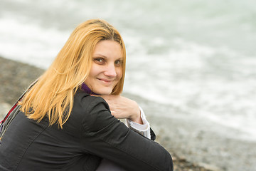 Image showing Portrait of sitting on the beach smiling young woman in cold weather