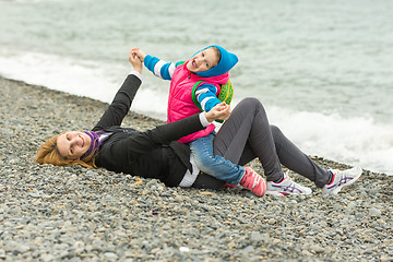 Image showing Five-year girl with her mother having fun on the beach pebble beach in cold weather