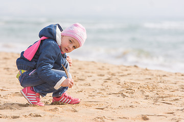 Image showing Five-year girl in the spring of the pen draws on the sand by the sea, and looked into the frame