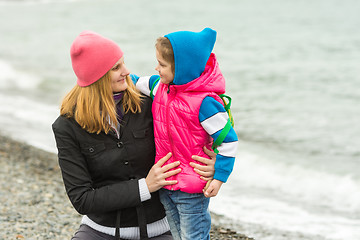 Image showing  Mother hugging little daughter and tenderly looking at her on the beach in cold weather