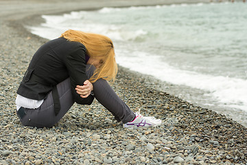 Image showing Girl in a cool day on the beach sits thoughtfully with his face buried in his knees