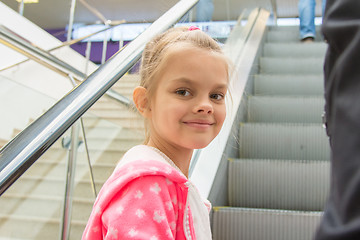 Image showing Seven-year girl lying down on an escalator in a mall with a smile look in the frame