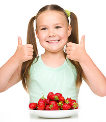 Image showing Happy little girl is eating strawberries