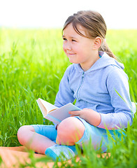 Image showing Little girl is reading a book outdoors